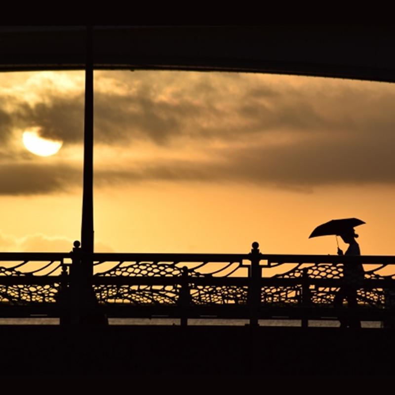 夕焼けの空の下、日傘を手に橋を歩く女性のシルエットが美しい秋の風景