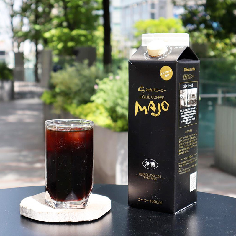 木漏れ日の屋外でグラスに注がれたアイスコーヒーとMAJOリキッドコーヒーのパッケージ